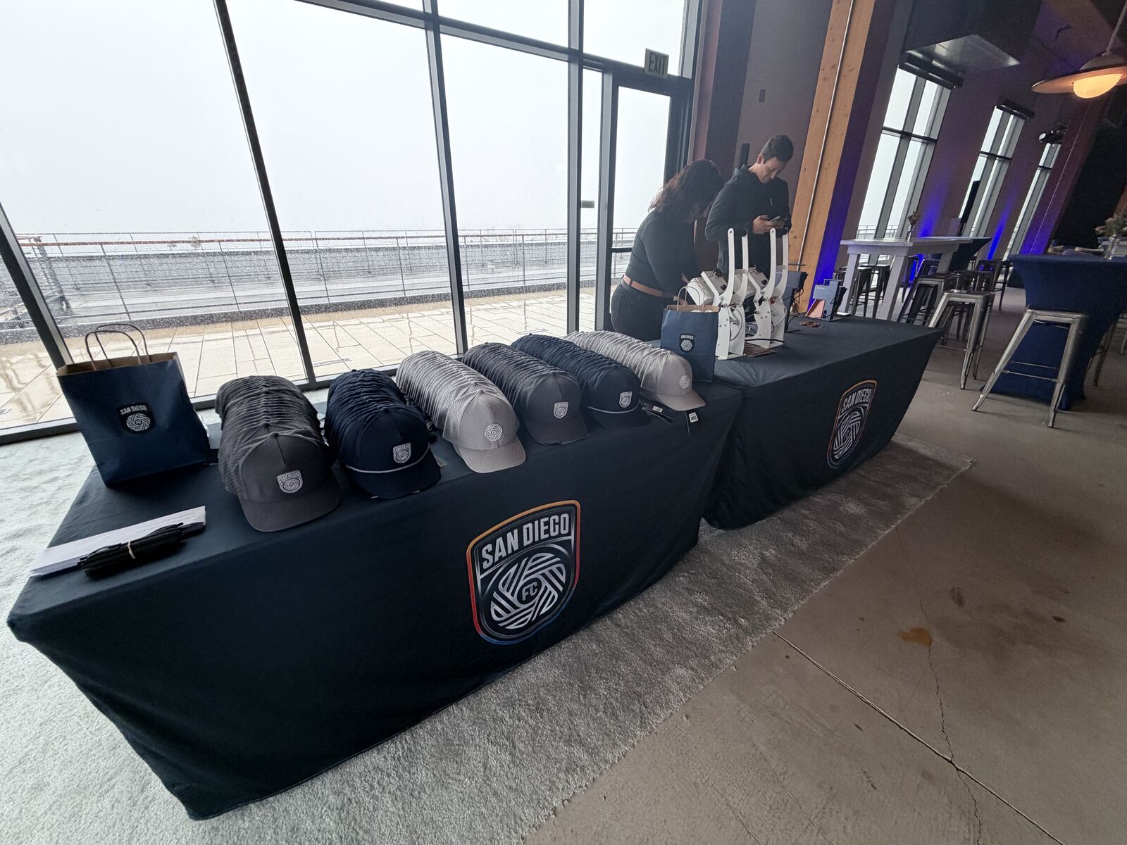Outdoor event booth with a tiered display of branded hats and apparel overlooking a city waterfront